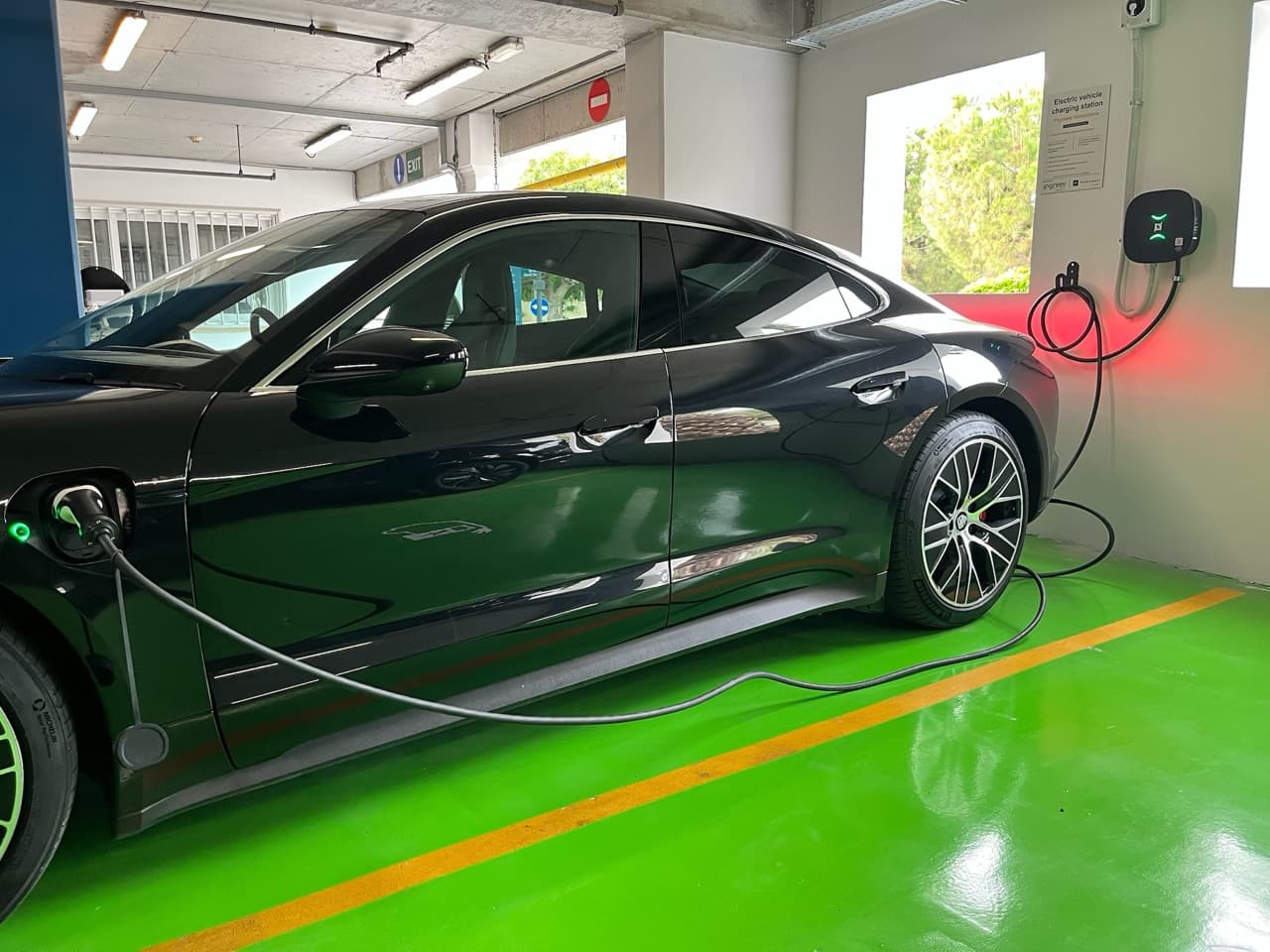 An electric car charging from a wall-mounted AC unit in a green-marked bay of the Limassol Marina parking garage