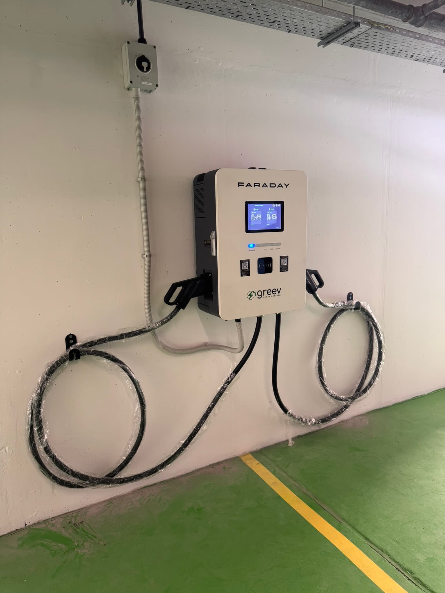 A wall-mounted DC fast charger with twin tethered connectors in the Limassol Marina parking garage